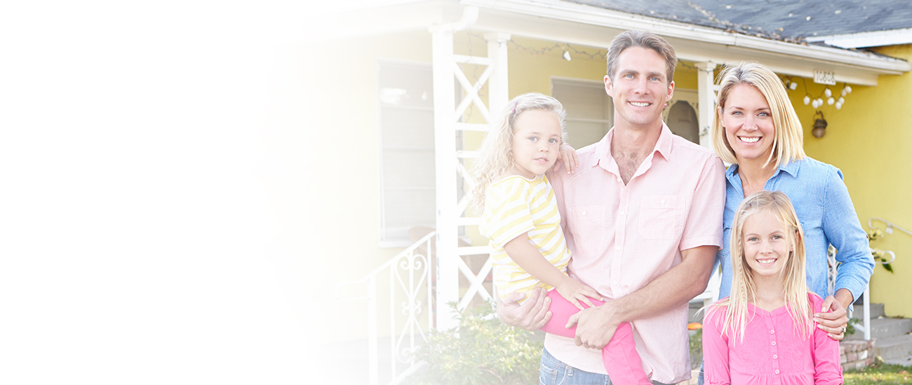 Photograph of a family: father, mother, and their 2 daughters, with their yellow house in the background.